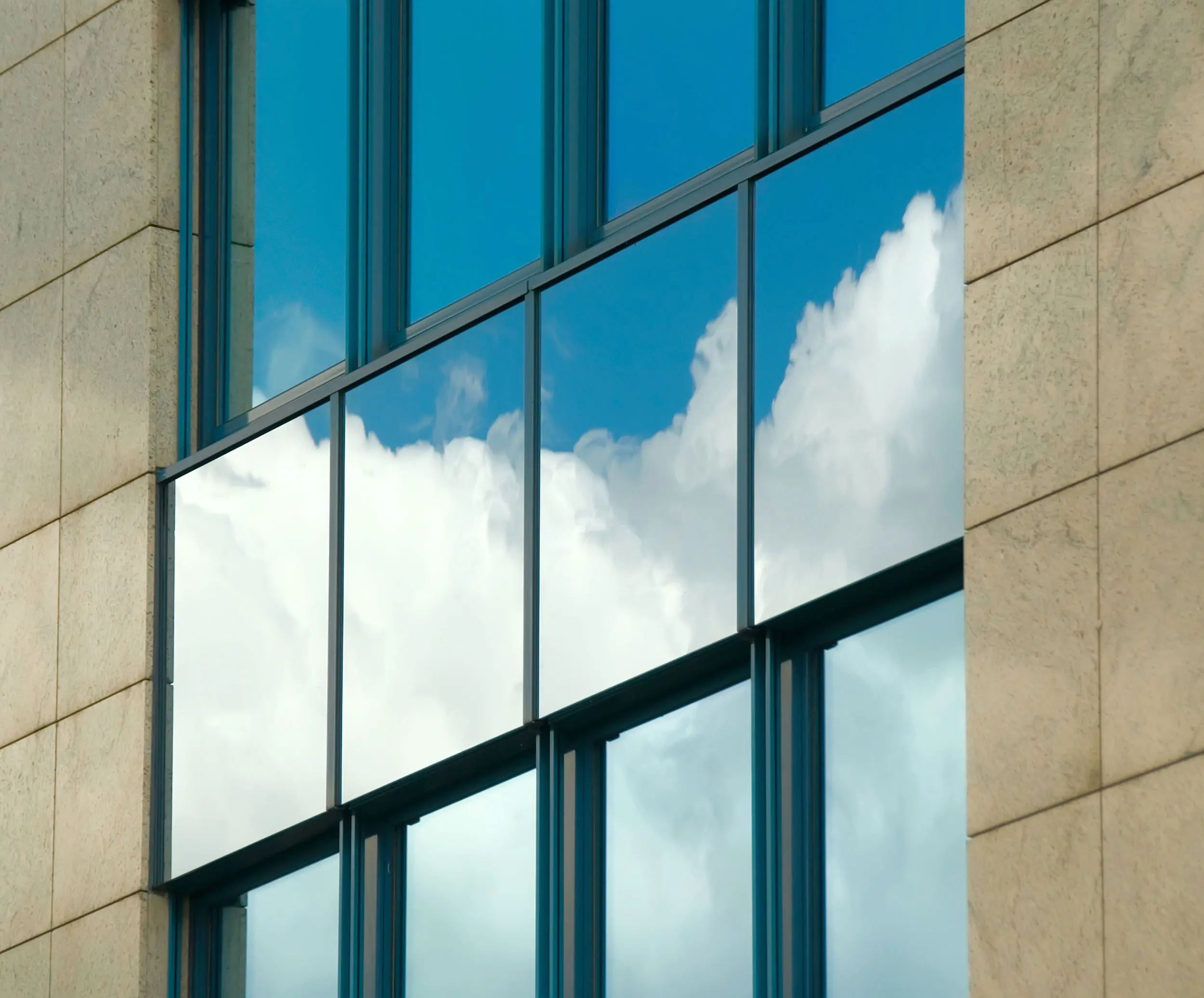 Bürofassade mit Haverkamp Silber Dunkel 20R SR Primus Folie spiegelt weiße Wolken und reduziert Hitzeeintrag.