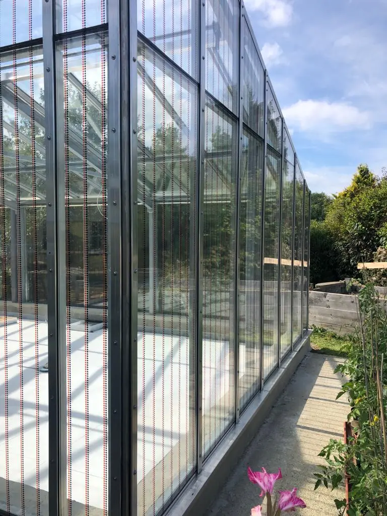 Gewächshaus mit Haverkamp birdsafe® Vogelschutzfolie mit Rautenmuster orange schwarz im sonnigen Garten.